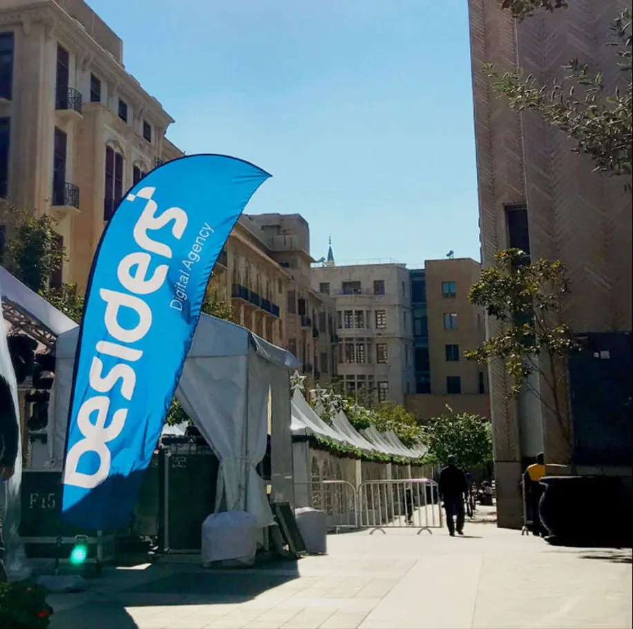 A blue Besiders flag on a pedestrian street in Beirut, between stone buildings on a sunny day